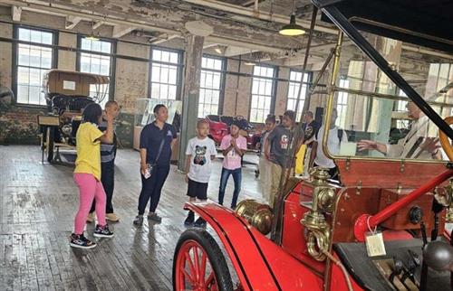 students inside the Ford playing looking at a red Model T